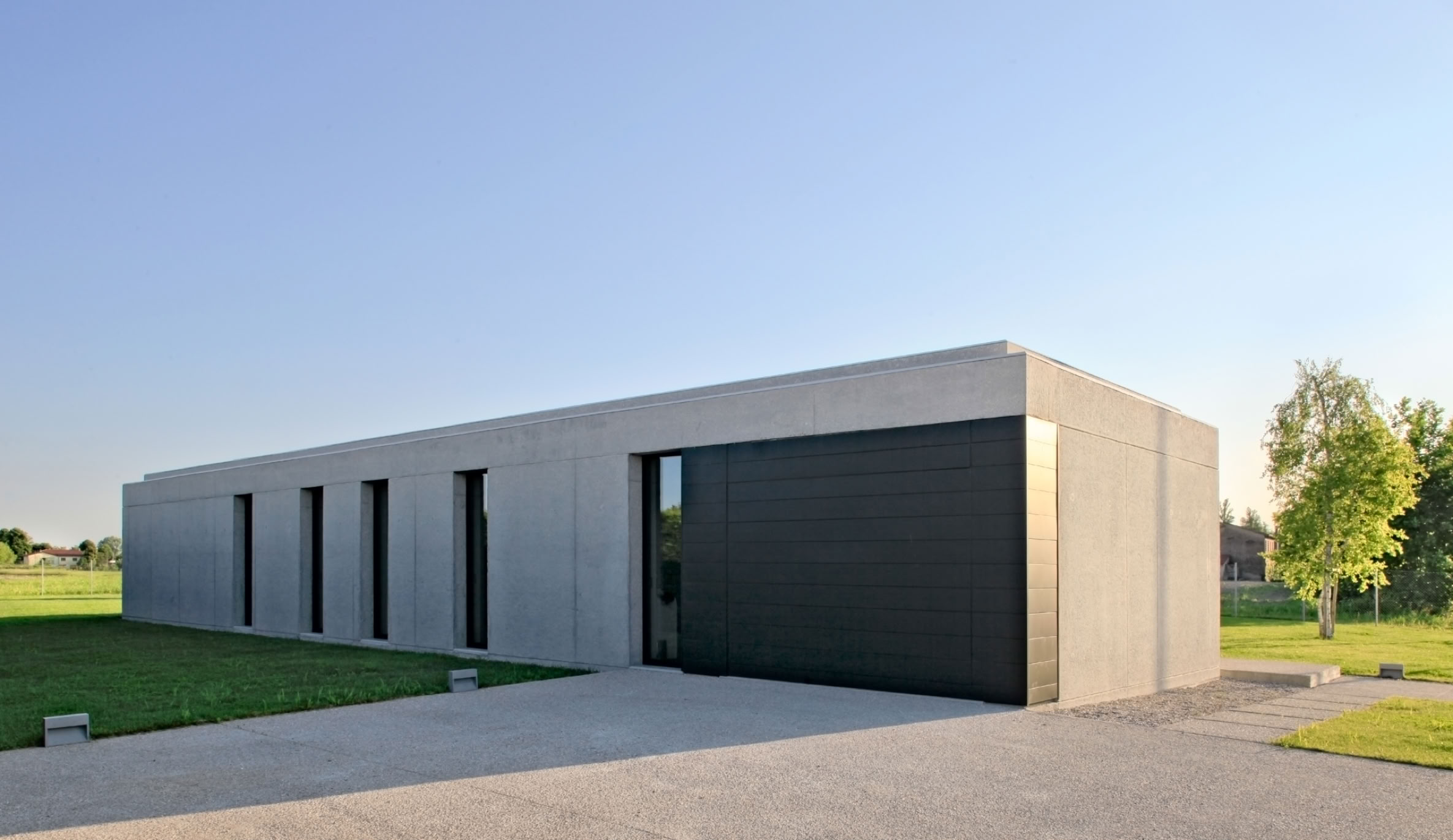 Villa unifamiliare su un unico piano progettata da MIDE architetti, con volumi essenziali in calcestruzzo sabbiato e ampie vetrate rivolte al giardino.