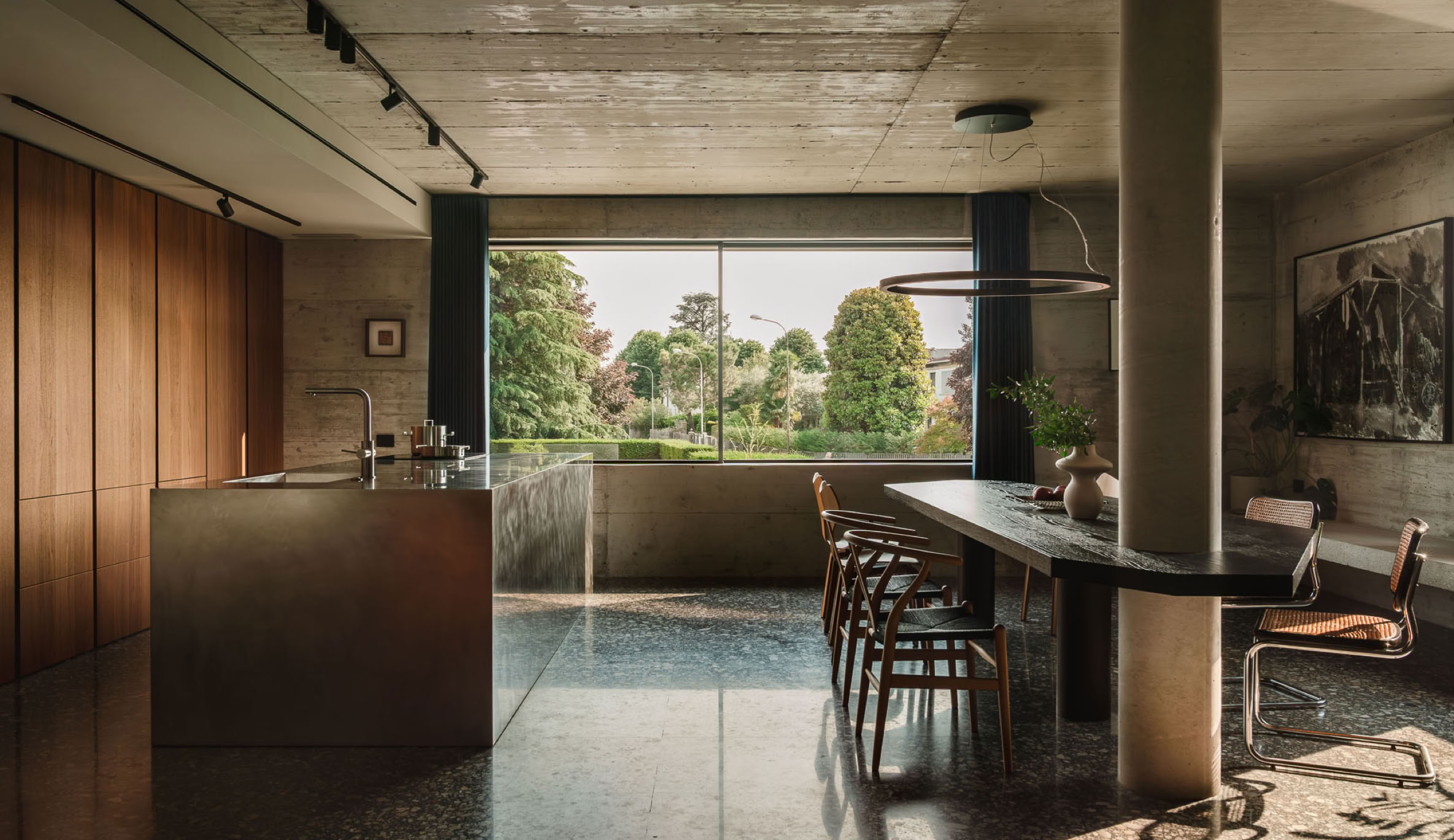 Vista della cucina contemporanea con isola e volume strutturale in calcestruzzo, elemento che definisce lo spazio e incornicia le funzioni.