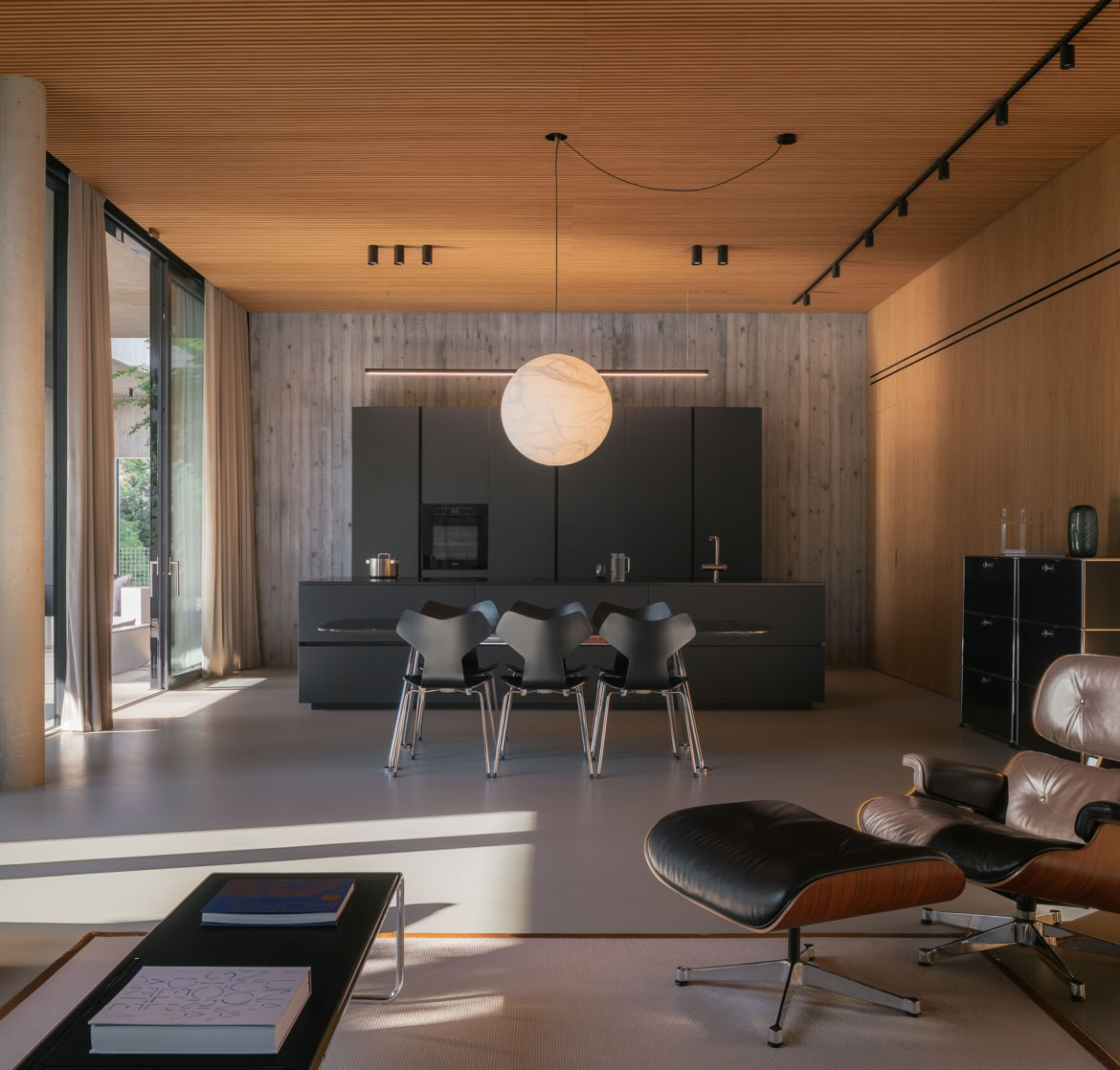 La cucina si integra armoniosamente con la zona living grazie all’uso coerente di colori neutri e materiali materici. Legno e resina a terra definiscono uno spazio fluido, funzionale e raffinato, senza soluzione di continuità visiva.