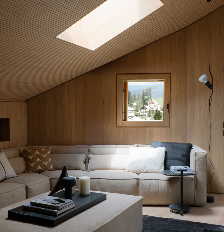 Ampio soggiorno arredato con divano e poltrone di design, caratterizzato da luce naturale e vista sulle Dolomiti.