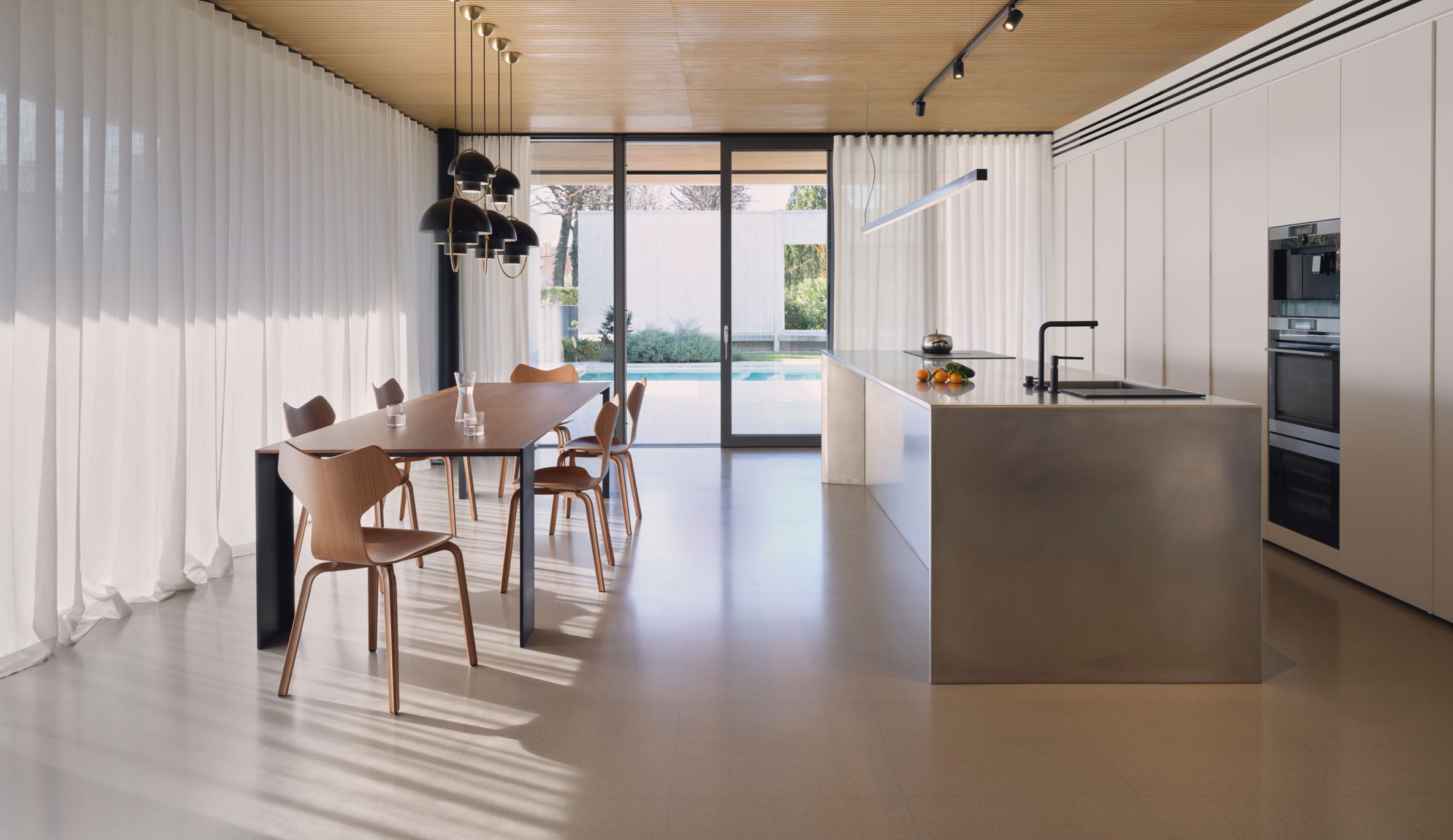 Vista della zona giorno con ampie vetrate che comunicano con il patio e la cucina esterni.