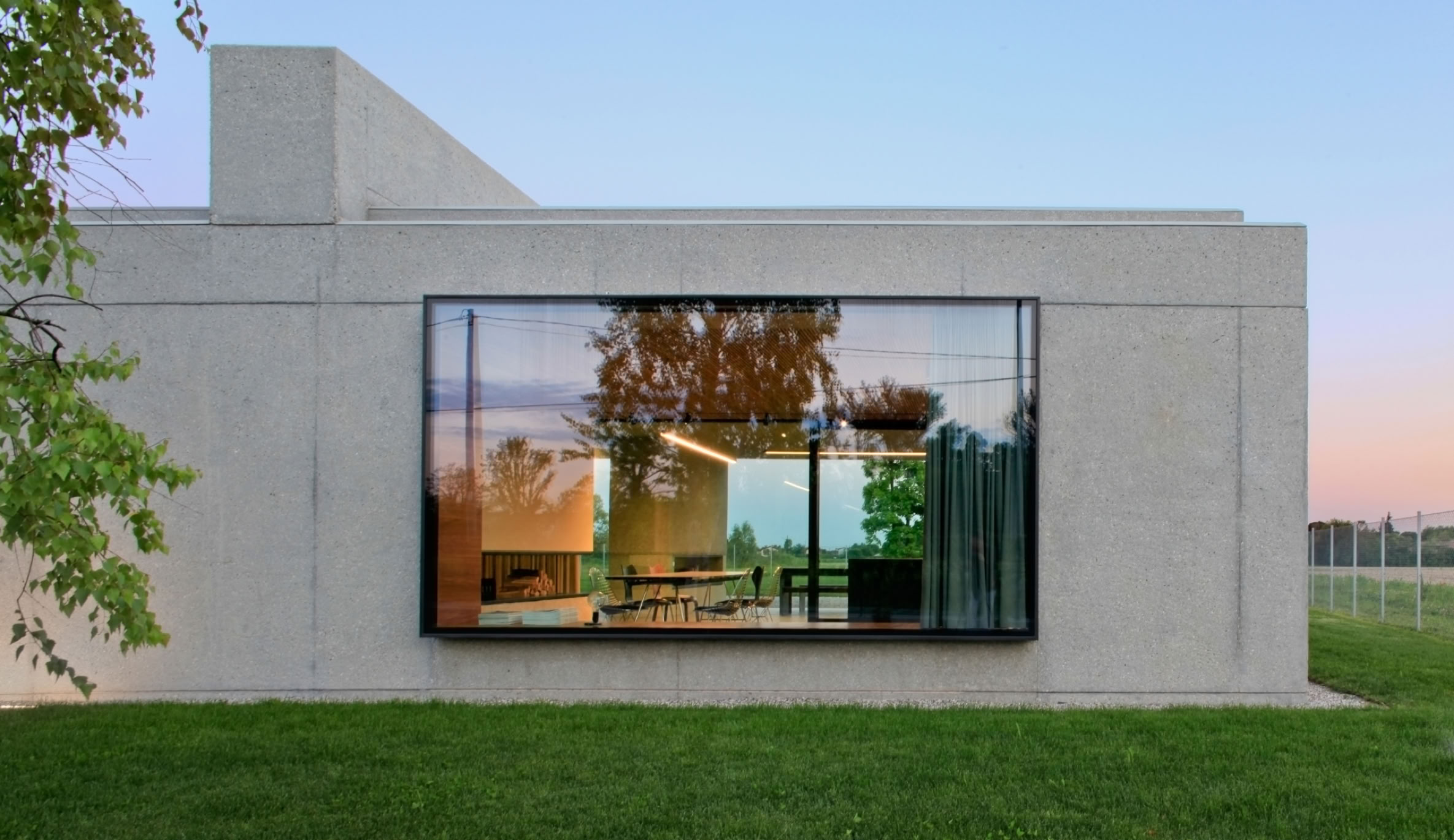 Villa unifamiliare su un unico piano progettata da MIDE architetti, con volumi essenziali in calcestruzzo sabbiato e ampie vetrate rivolte al giardino.