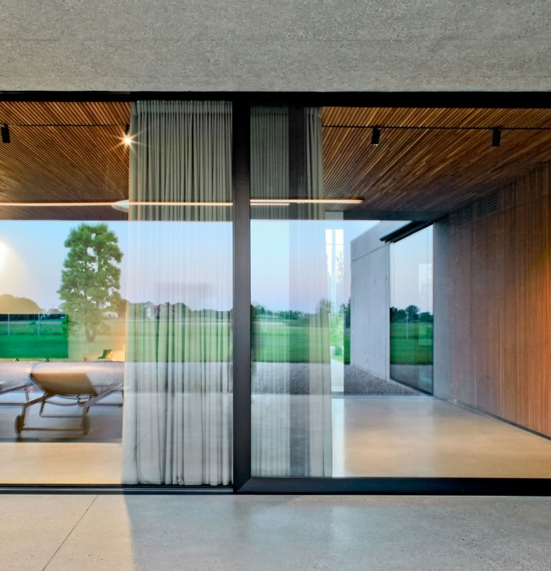 Villa unifamiliare su un unico piano progettata da MIDE architetti, con volumi essenziali in calcestruzzo sabbiato e ampie vetrate rivolte al giardino.