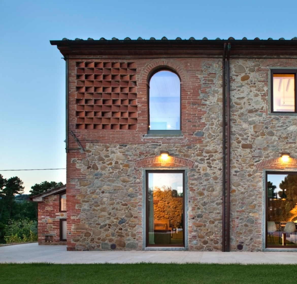 Facciata in pietra e mattone faccia a vista, con infissi in acciaio e scuri in legno che valorizzano l’architettura tradizionale toscana.