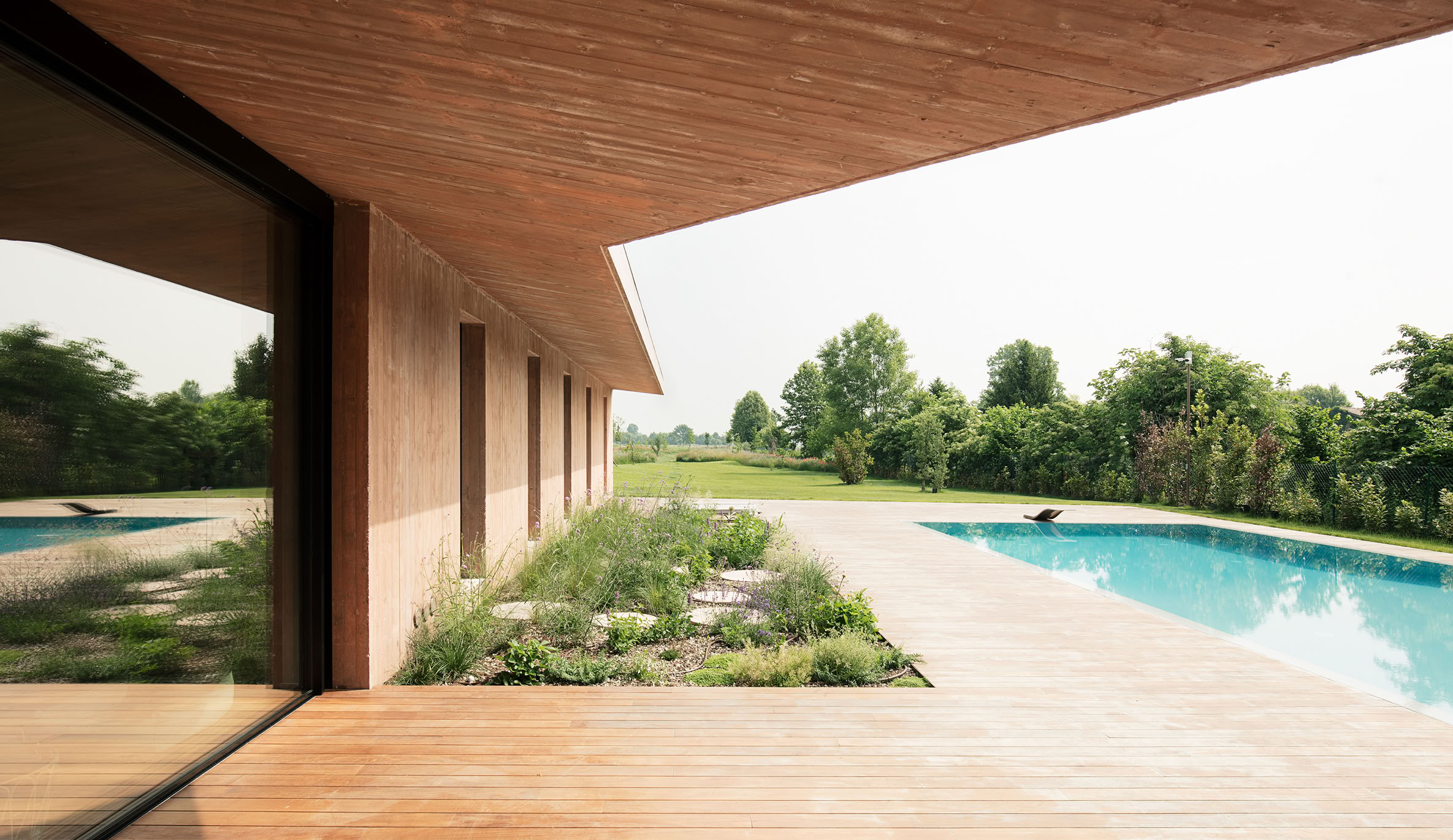 Vista dal portico della zona solarium e della piscina a sfioro progettate da MIDE architetti per un benessere abitativo dalle esigenze contemporanee.